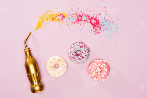 Preview: Top view of three frosted donuts and golden bottle on pink surface. Colorful donuts chocolate