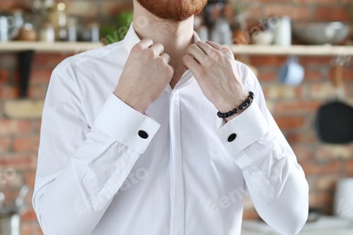 Preview: Man Fastening Shirt in Modern Kitchen Setting