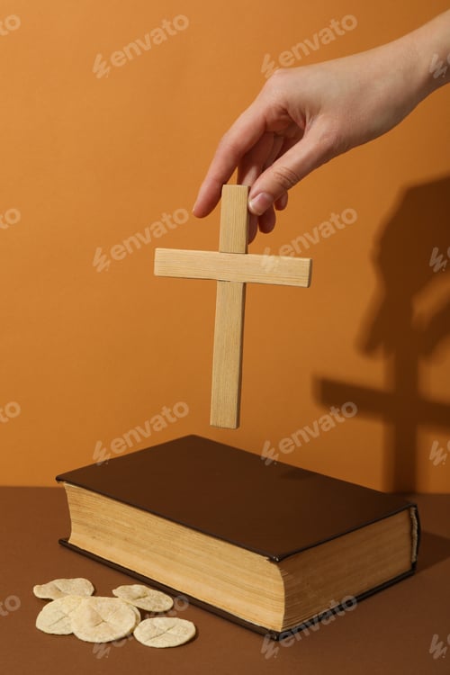 Preview: Bread, wooden cross in hand and Bible on orange background