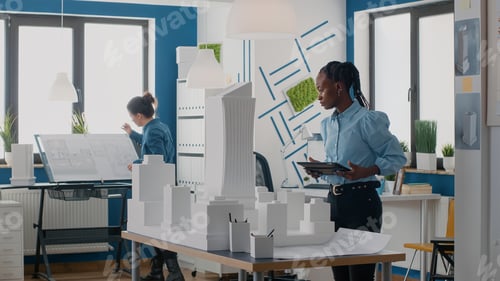 Preview: African american architect working with digital tablet to design blueprints plan and building model