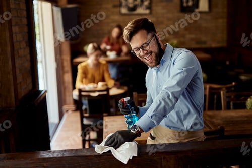 Preview: Young cheerful waiter having fun while cleaning cafe.