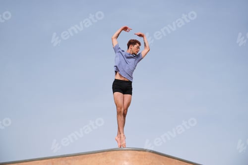 Preview: Ballet dancer is performing en pointe on a concrete structure with the sky in the background