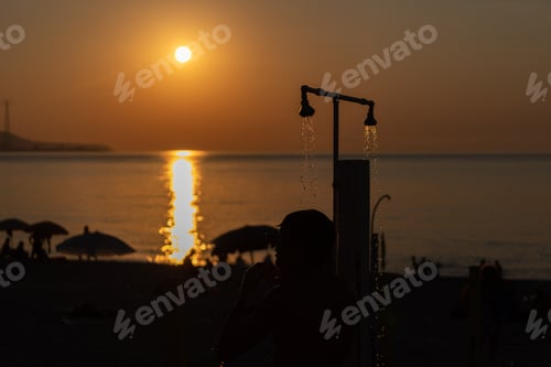 Preview: Man silhouette taking shower after swimming at the sea beach. Beautiful view of orange sunset