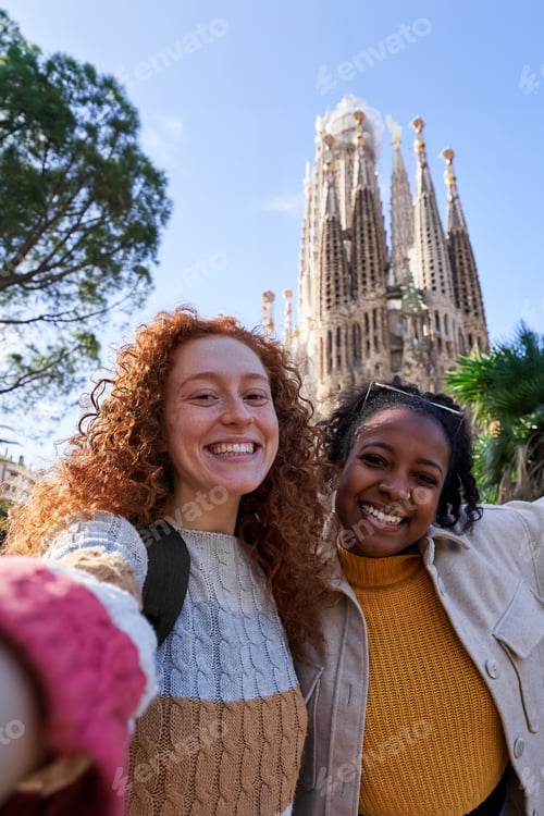 Preview: Two happy tourists taking a selfie with sagrada familia in background during a sunny day.
