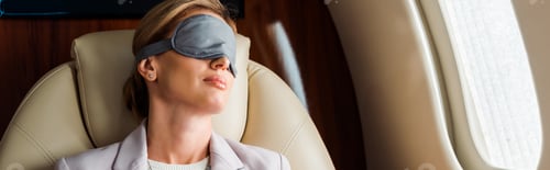 Preview: panoramic shot of businesswoman with sleeping mask sitting in private plane