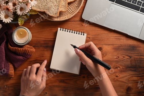 Preview: Creative woman holding pen and writing on empty notebook.