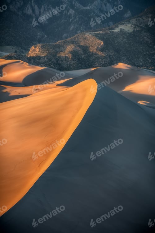 Preview: Vertical shot of sand dunes with mountains in the background at daytime