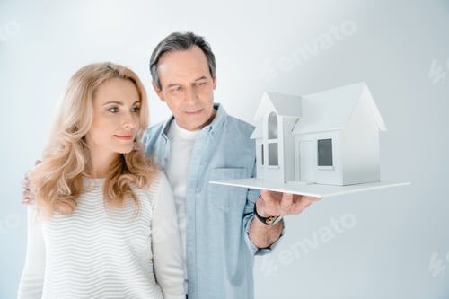 Preview: portrait of mature couple looking at house model isolated on grey