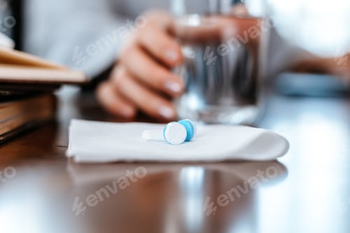 Preview: white round pill on tissue and blur hand take a glass of water.