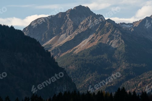 Preview: Aerial view of steep rocky mountains with green trees and forests under blue cloudy sky