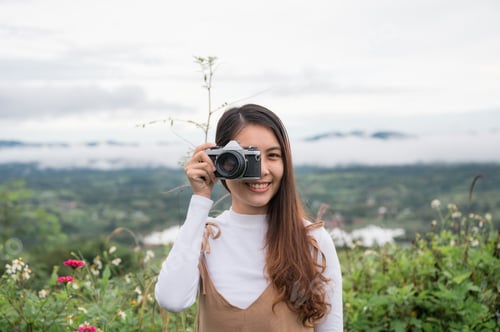 Preview: Young asian woman taking photo with retro film camera among the nature in the morning