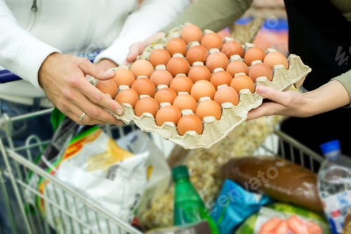 Preview: Happy young family standing near the counter with eggs in the supermarket