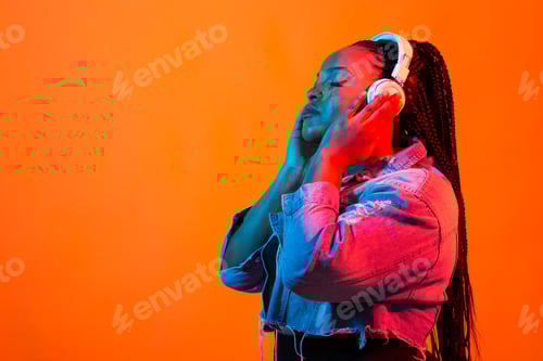 Visualização: Jovem afro-americana ouvindo música online dançando e cantando com fones de ouvido, néon