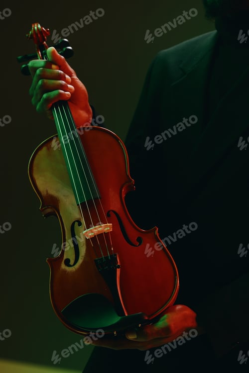 Preview: Mysterious man in black suit playing violin in front of vibrant green and red background, close up