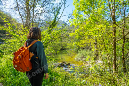 Preview: A young woman with a backpack looking at the mountains and the Sella river between El Tornin