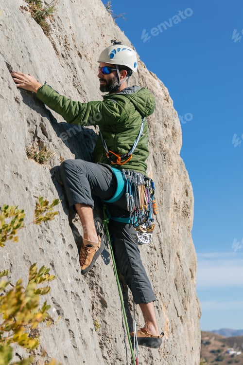 Preview: Man climbing steep cliff on cloudless day