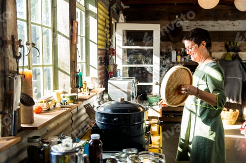 Preview: Mature woman cooking with food steamer in kitchen