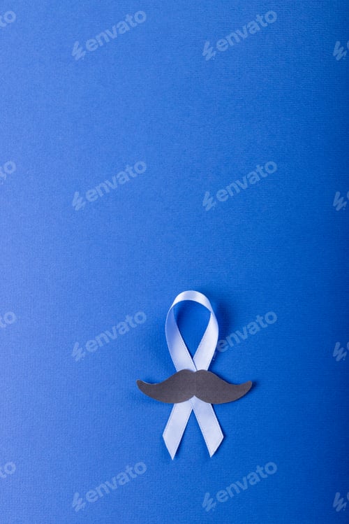 Preview: Directly above shot of prostate cancer awareness blue ribbon with paper mustache on blue background