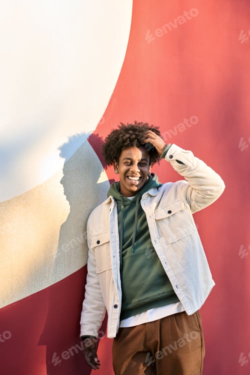 Preview: Happy African American teen guy laughing standing at red wall. Vertical