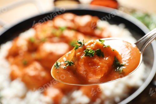 Preview: Tasty butter chicken in spoon over dish with meal, closeup