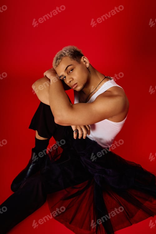 Preview: Trendy young man in tank top showcasing modern style against vibrant red backdrop