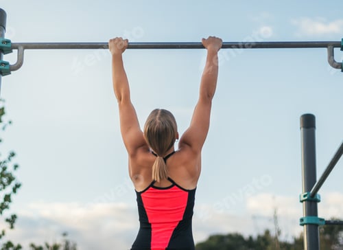 Preview: back view of a woman athlete doing pull ups on a bar outdoors. calisthenics