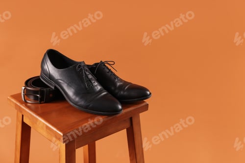 Preview: Pair of black leather shoes on stool against brown background. Space for text