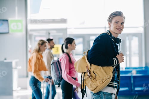 Preview: handsome young man with backpack smiling at camera while traveling with friends