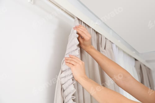 Preview: Woman hanging window curtain indoors, closeup. Interior decor element