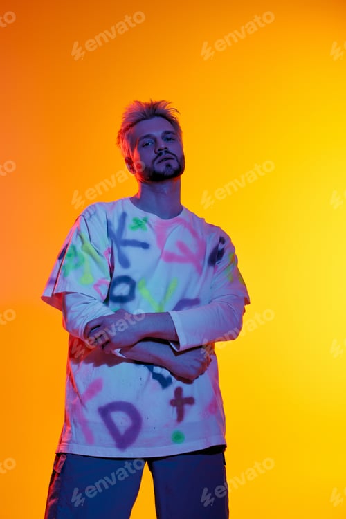 Vista previa: Handsome young man poses confidently against vibrant orange backdrop with creative style