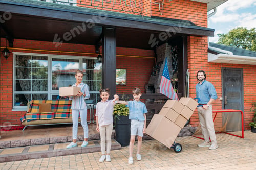 Preview: children with keys and parents with cardboard boxes standing at country house, moving home concept