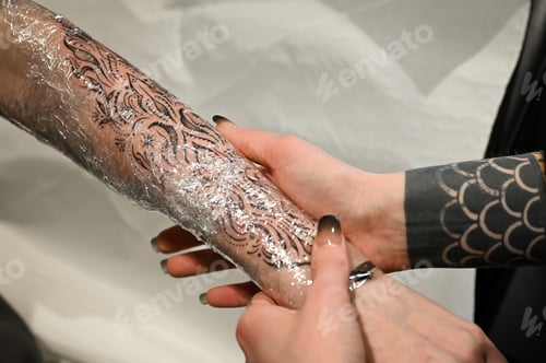 Preview: Tattoo artist wrapping a new tattoo with protective film