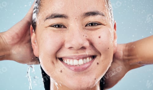 Preview: Face, shower and happy woman cleaning hair in studio isolated on blue background. Water splash, hyg