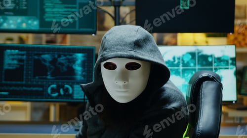 Preview: Masked hacker in his apartment looking into the camera
