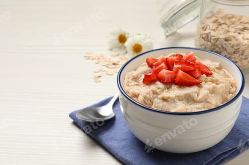 Preview: Tasty oatmeal porridge with strawberries served on white wooden table. Space for text