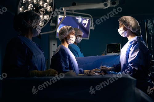 Preview: Team of surgeons in operating uniform stands at surgical table