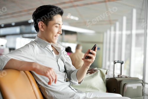 Preview: Young Chinese man with smart phone waiting in airport lounge