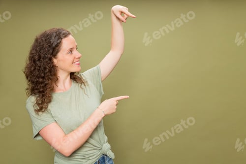 Preview: Portrait young redhead girl pointing fingers in the air wearing green t-shirt on green background