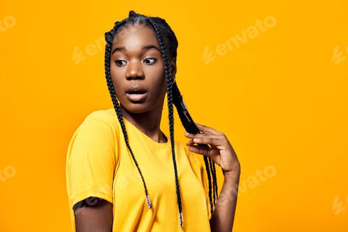 Preview: A surprised young Black woman with braided hair, wearing a bright yellow t shirt, posed against a