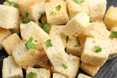 Preview: Tasty crispy croutons with cut parsley on black wooden table, closeup