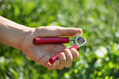 Preview: Sports red metal expander in man's hand.