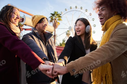Preview: Group of cheerful multiracial friends bump fists with a smile at amusement park in winter season