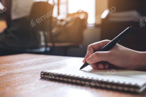 Preview: Closeup image of a hand writing down on a white blank notebook on wooden table