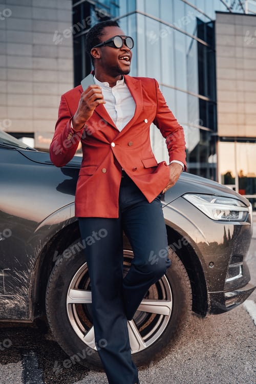 Preview: Cheerful african businessperson with phone and car outside