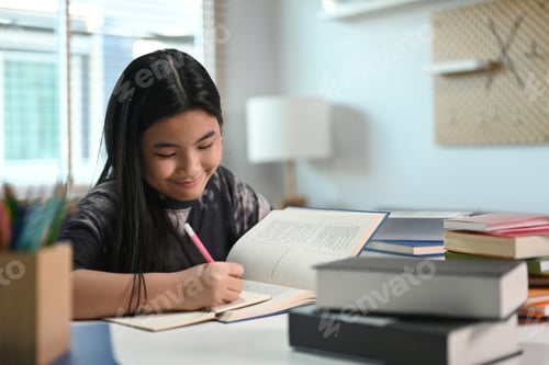 Preview: Smiling teenage girl doing homework at home.