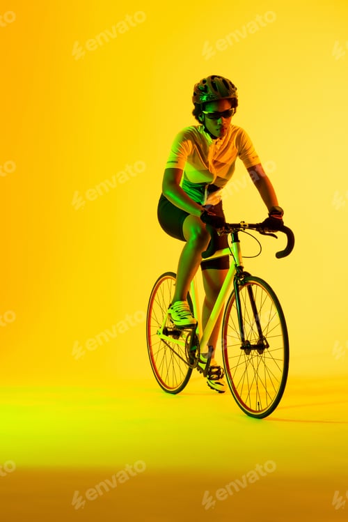 Preview: Vertical image of african american female cyclist riding bike in yellow lighting