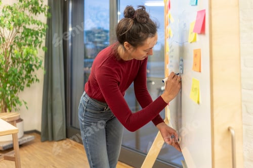 Preview: Mid adult businesswoman writing on office whiteboard