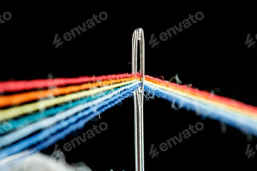 Preview: multi-colored threads for sewing in the form of a rainbow pass through an antique needle