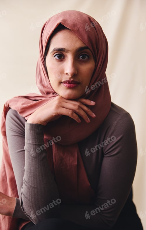 Preview: Portrait of young Muslim woman wearing hijab looking towards camera with hand on chin