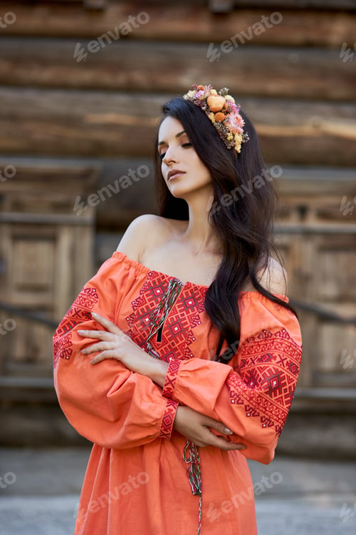 Preview: Beautiful Slavic woman in an orange ethnic dress and a wreath of flowers on her head. Beautiful